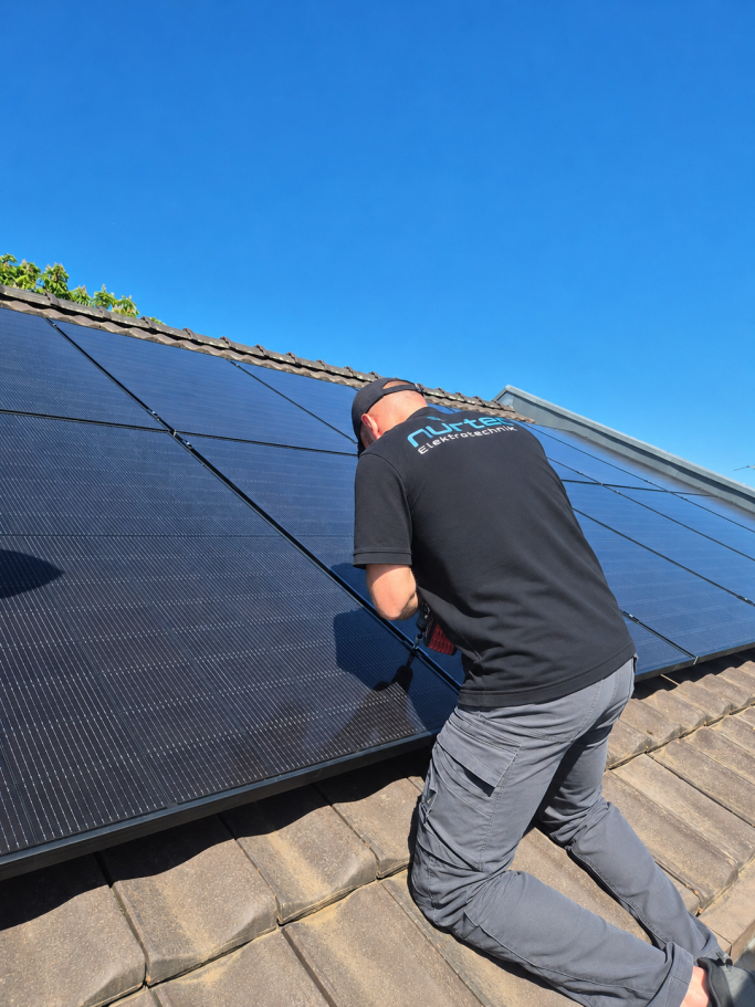 Monteur von rurtec in Firmenkleidung bei der Montage von Photovoltaik-Modulen auf einem Ziegeldach
