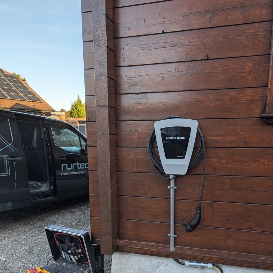 Von rurtec installierte Wallbox an einer Hausfassade, Firmenfahrzeug und Dach-Photovoltaik im Hintergrund